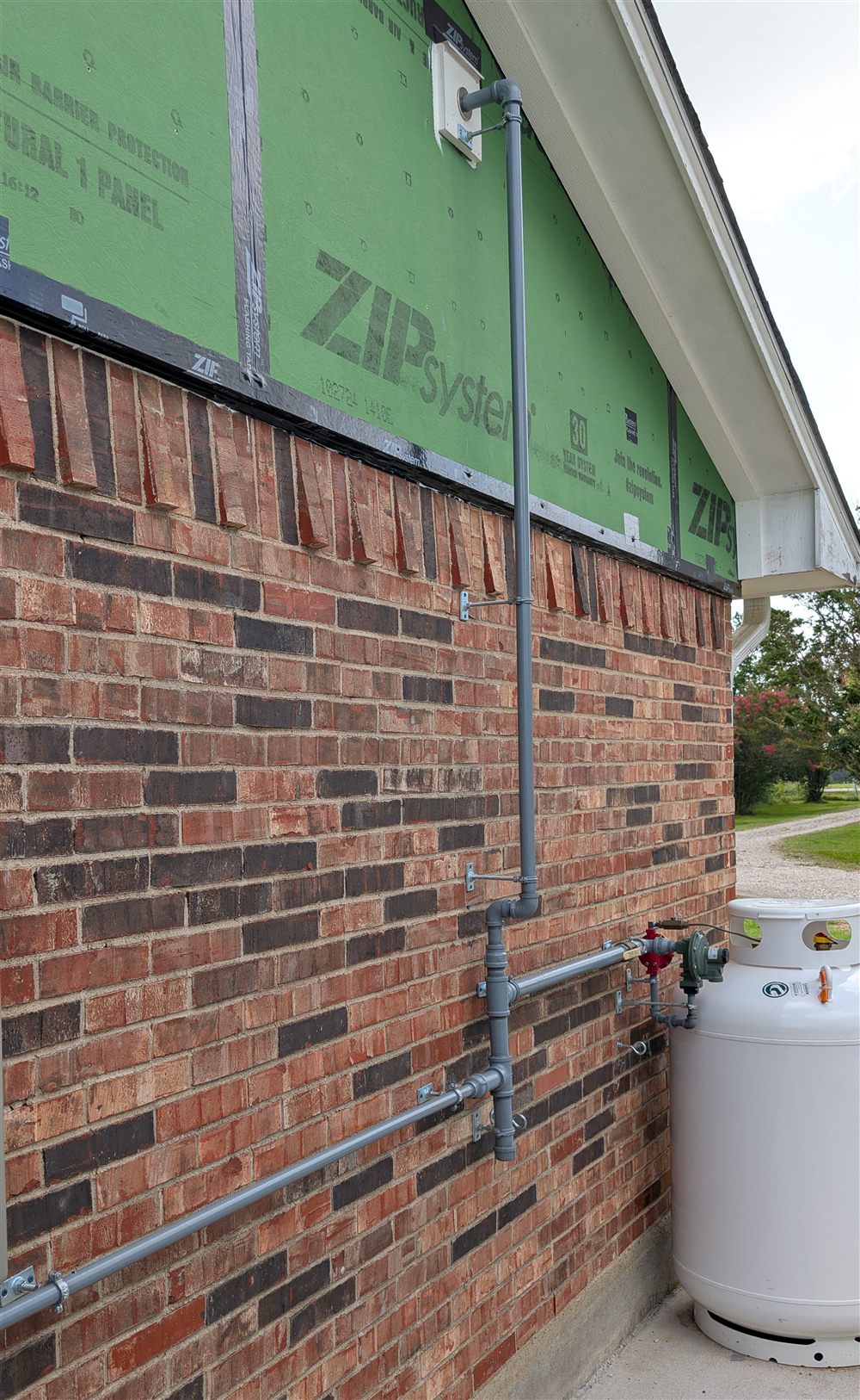 Fuel gas piping at an exterior tank connection mounted to a brick wall.