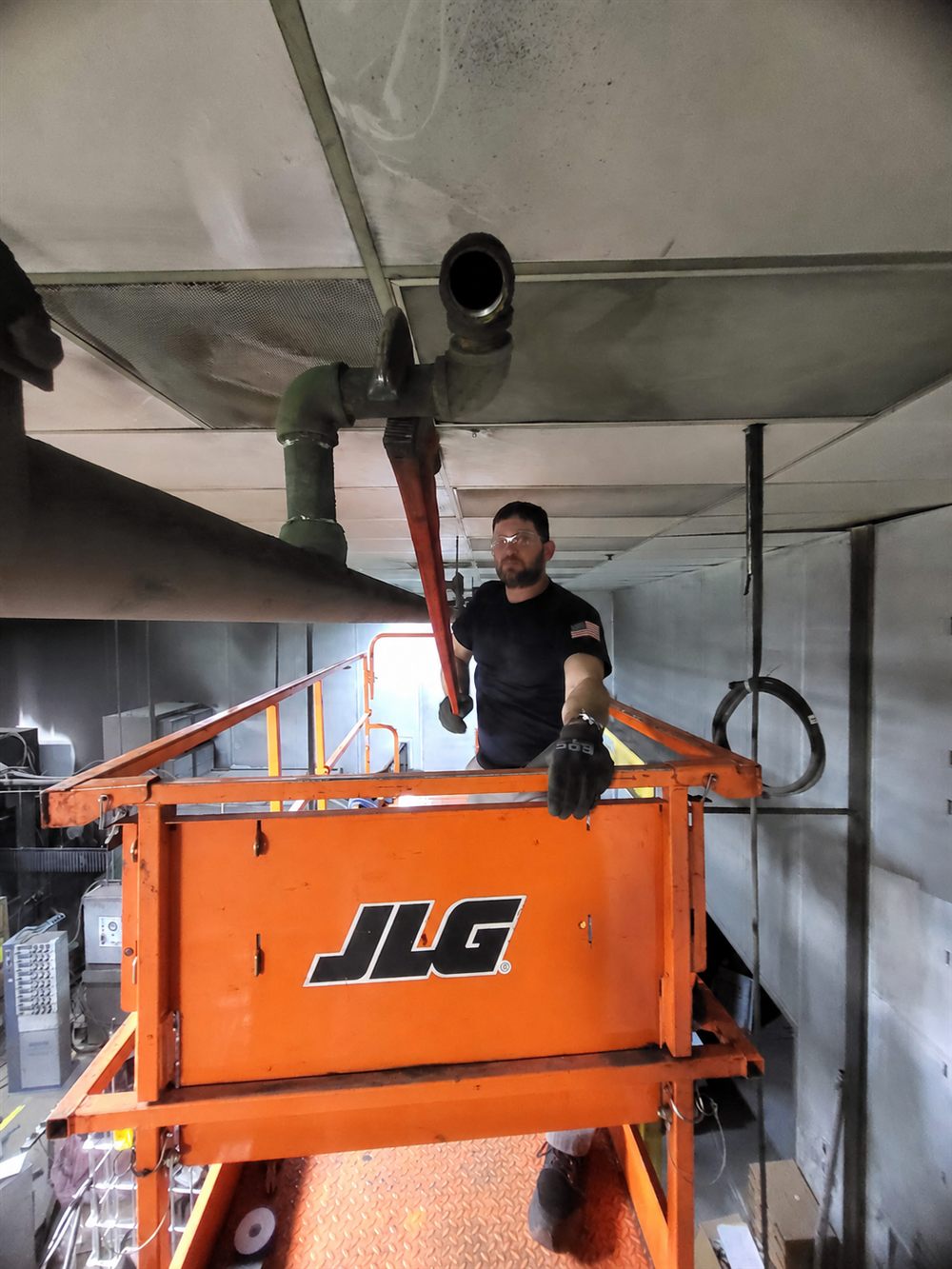 Technician on a lift using a wrench near overhead piping.