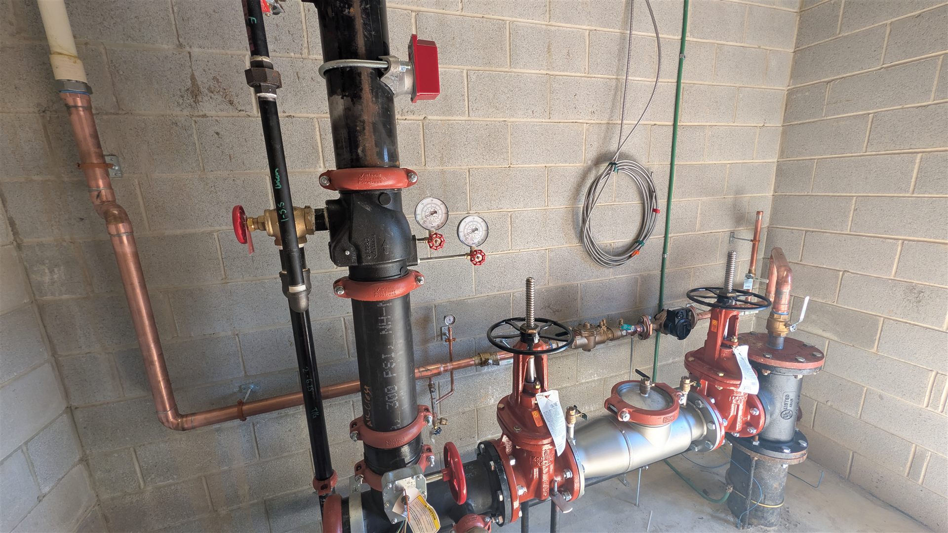 Backflow preventers, valves, gauges, and copper lines in a service room.